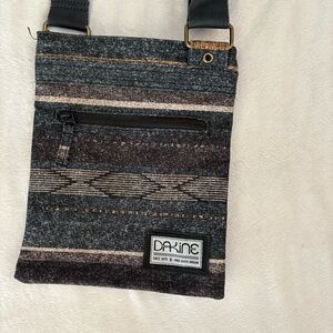 Dakine Jive crossbody bag in a dark grey with a multi-color striped pattern.
